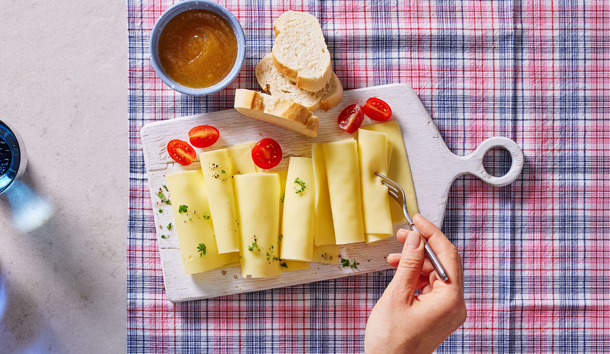 Ostskivor, körsbärstomater, bröd och sylt på en serveringsbräda.