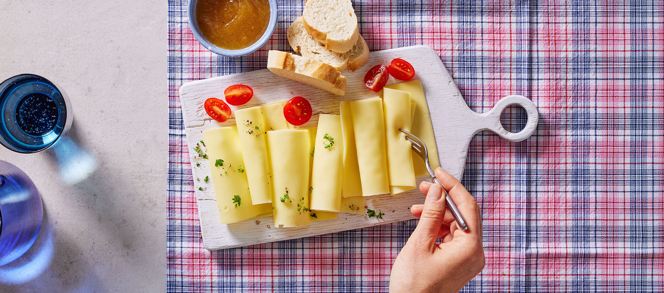 Ostskivor med körsbärstomater, bröd och sylt på en rutig duk.