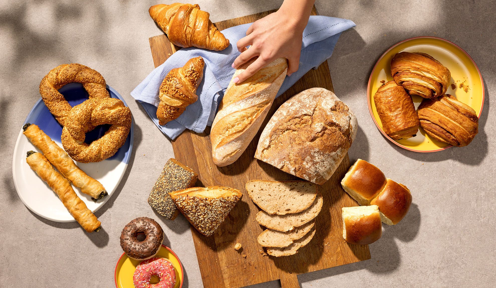 Sortiment av färska bakverk inklusive bröd, croissanter, bakelser och munkar på ett bord.
