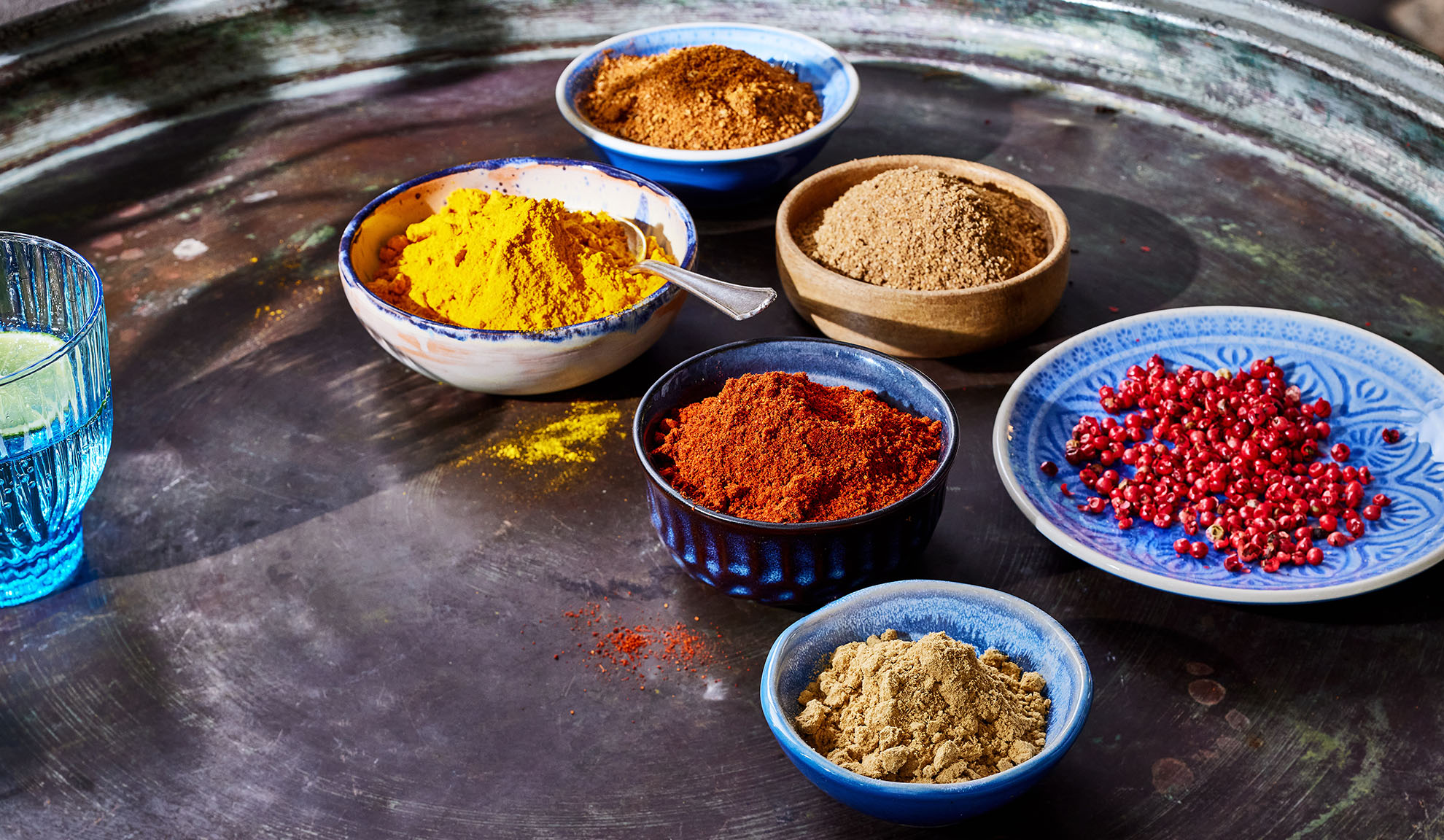 Olika kryddor i skålar: gurkmeja, paprika, peppar och andra på en metallbricka.