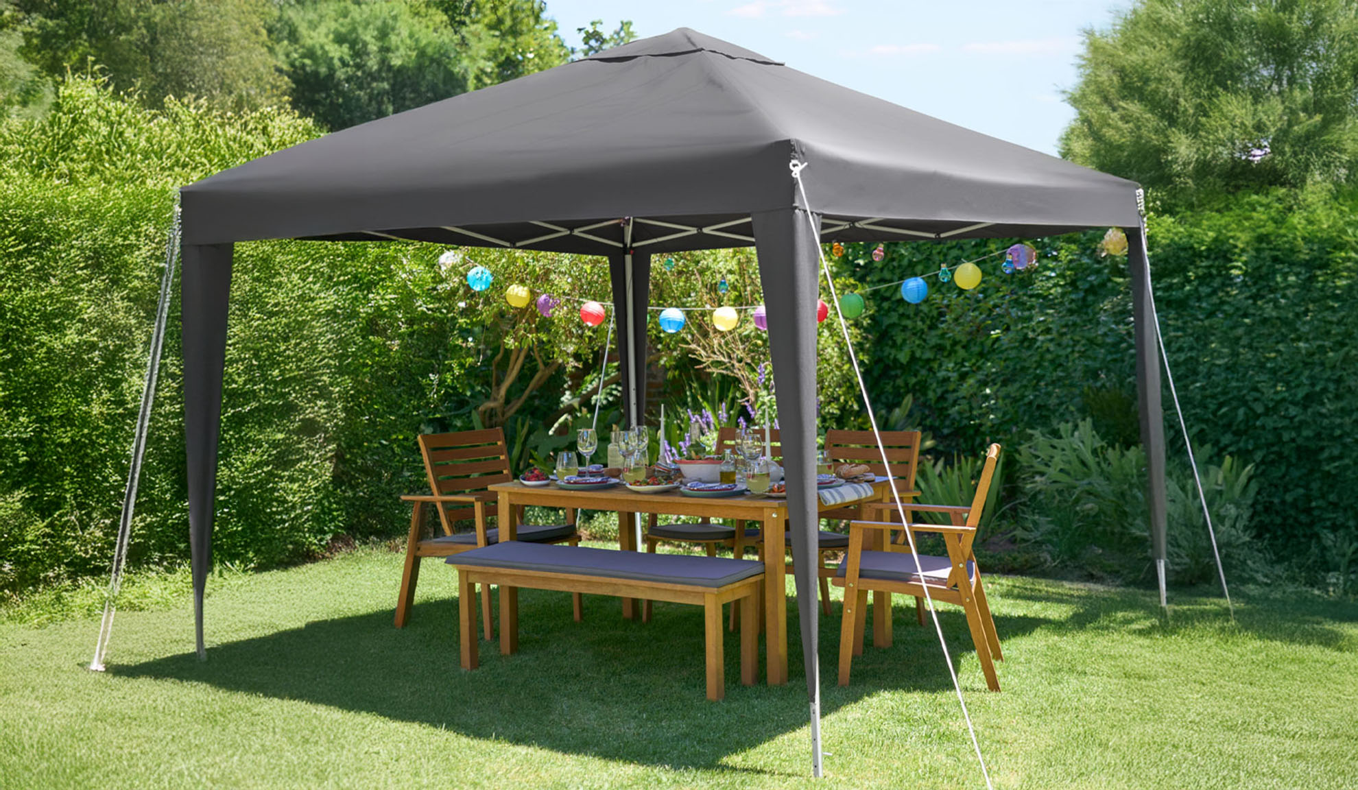 Mörkgrå trädgårdsgazebo med träbord och stolar.