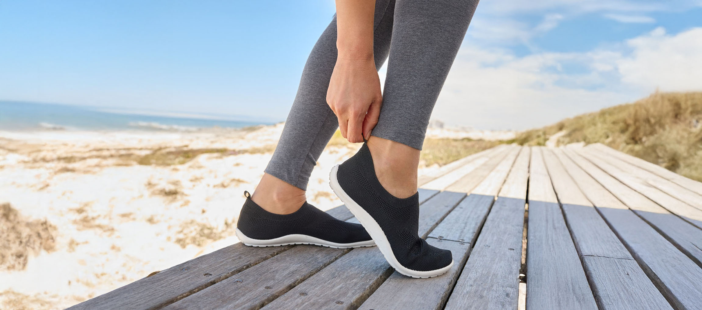 Kvinna som sätter på sig svarta sneakers vid havet.