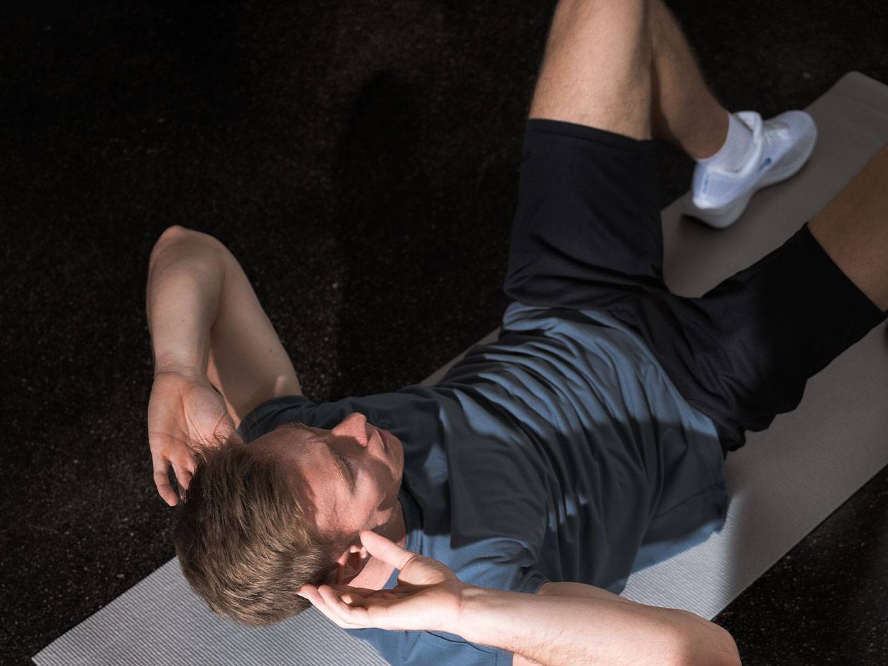 Man i blå t-shirt och svarta shorts gör situps på en yogamatta.