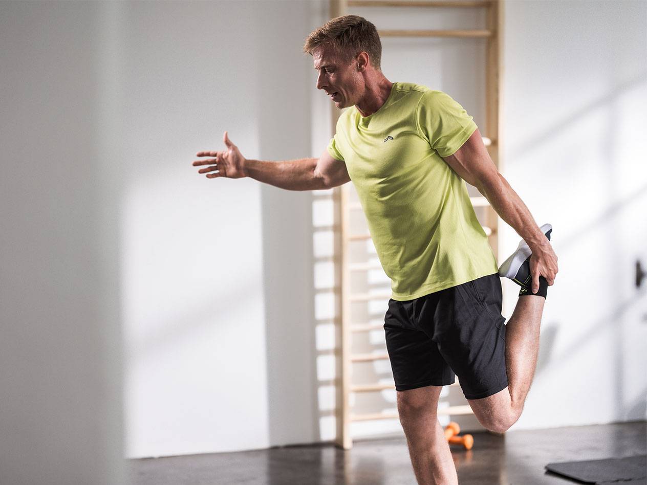 Man stretchar i svarta shorts och en limegrön t-shirt på ett gym.