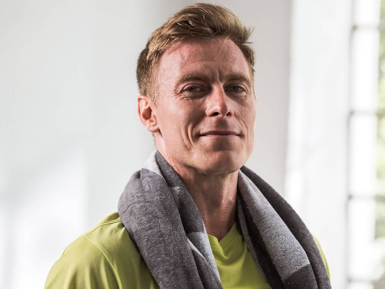 En blond man med en handduk runt halsen tittar in i kameran.