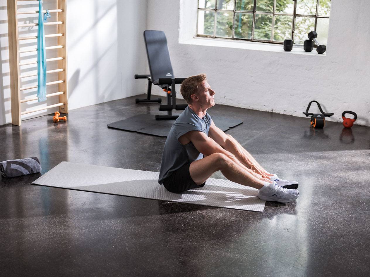 En man stretchar på en yogamatta i ett gym med utrustning.