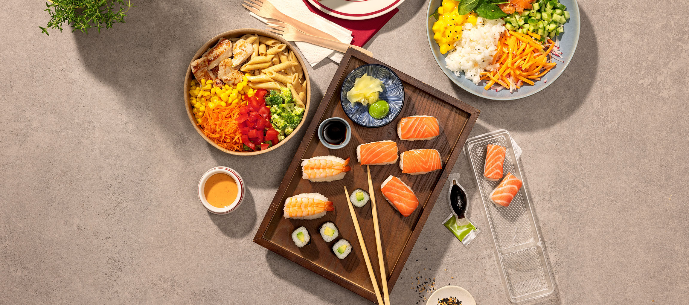Blandade rätter: pasta- och kycklingskål, sushi och en poke bowl på ett bord.