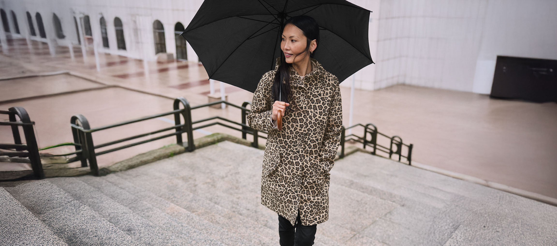 Kvinna i leopardmönstrad kappa med paraply på trappa.