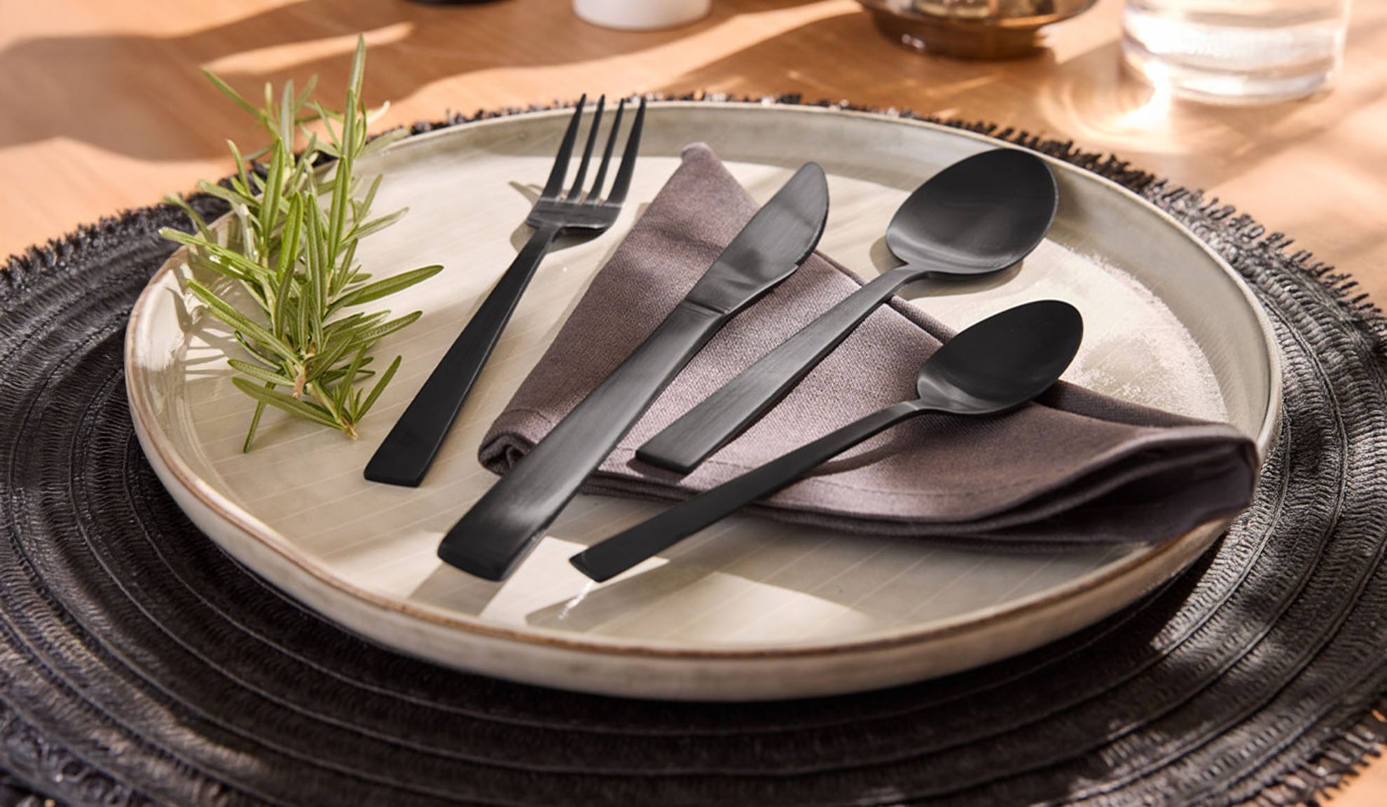 Svart bestickset med tallrik, servett och rosmarinkvist på en bordstablett.