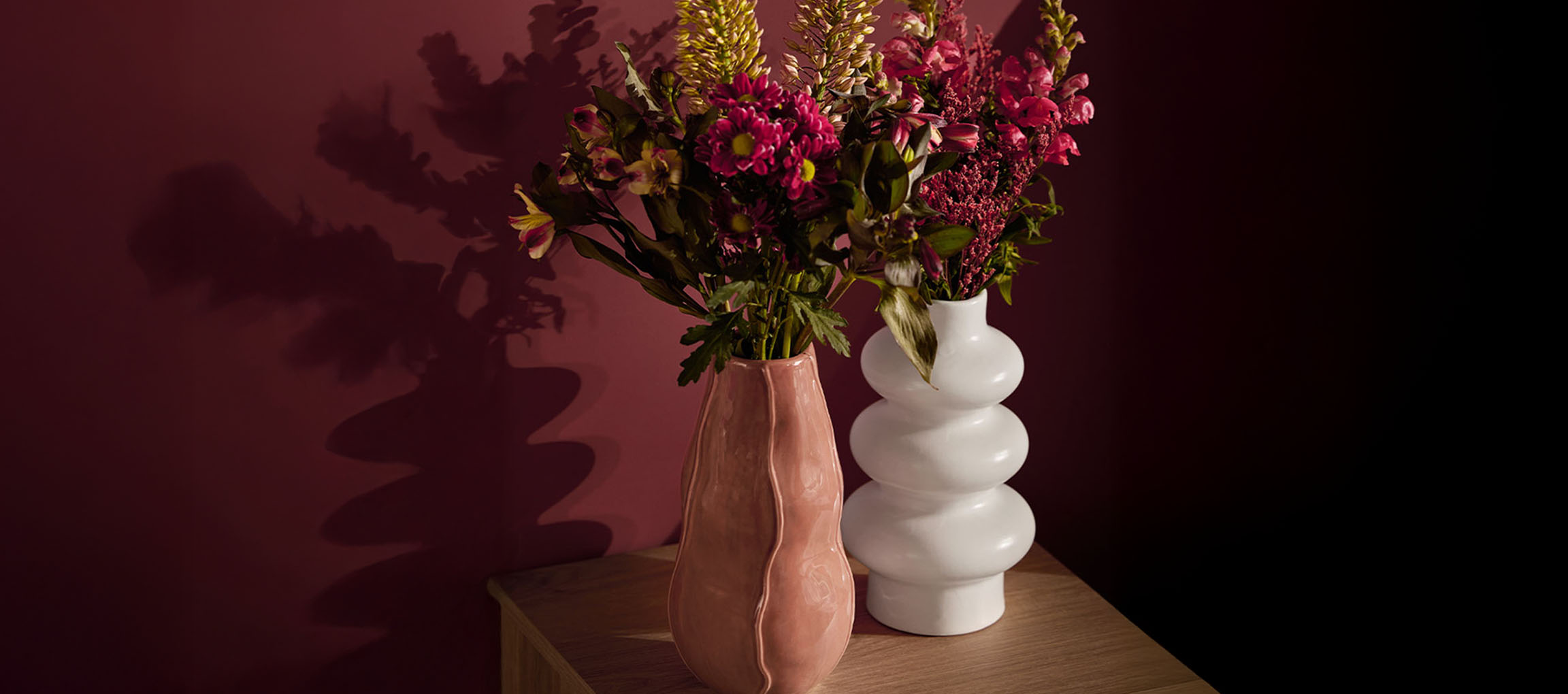 Två vaser med blommor, en rosa och en vit, på en träyta.