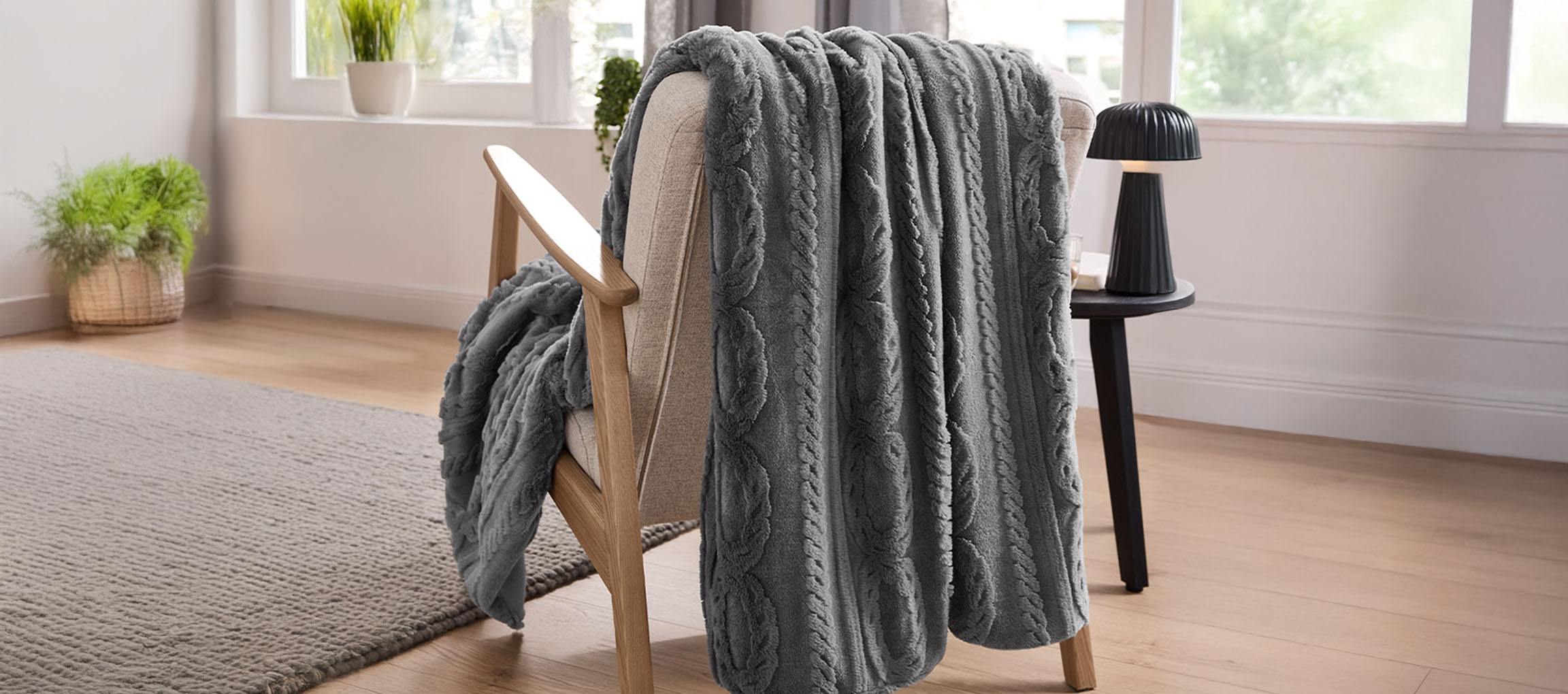Grå kabelstickad pläd draperad över en ljus träfåtölj i ett ljust rum.