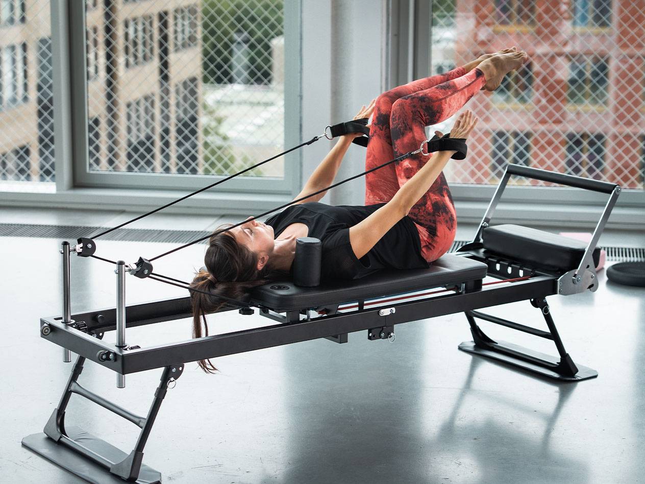 Kvinna tränar Pilates på en reformer med röda yogabyxor.