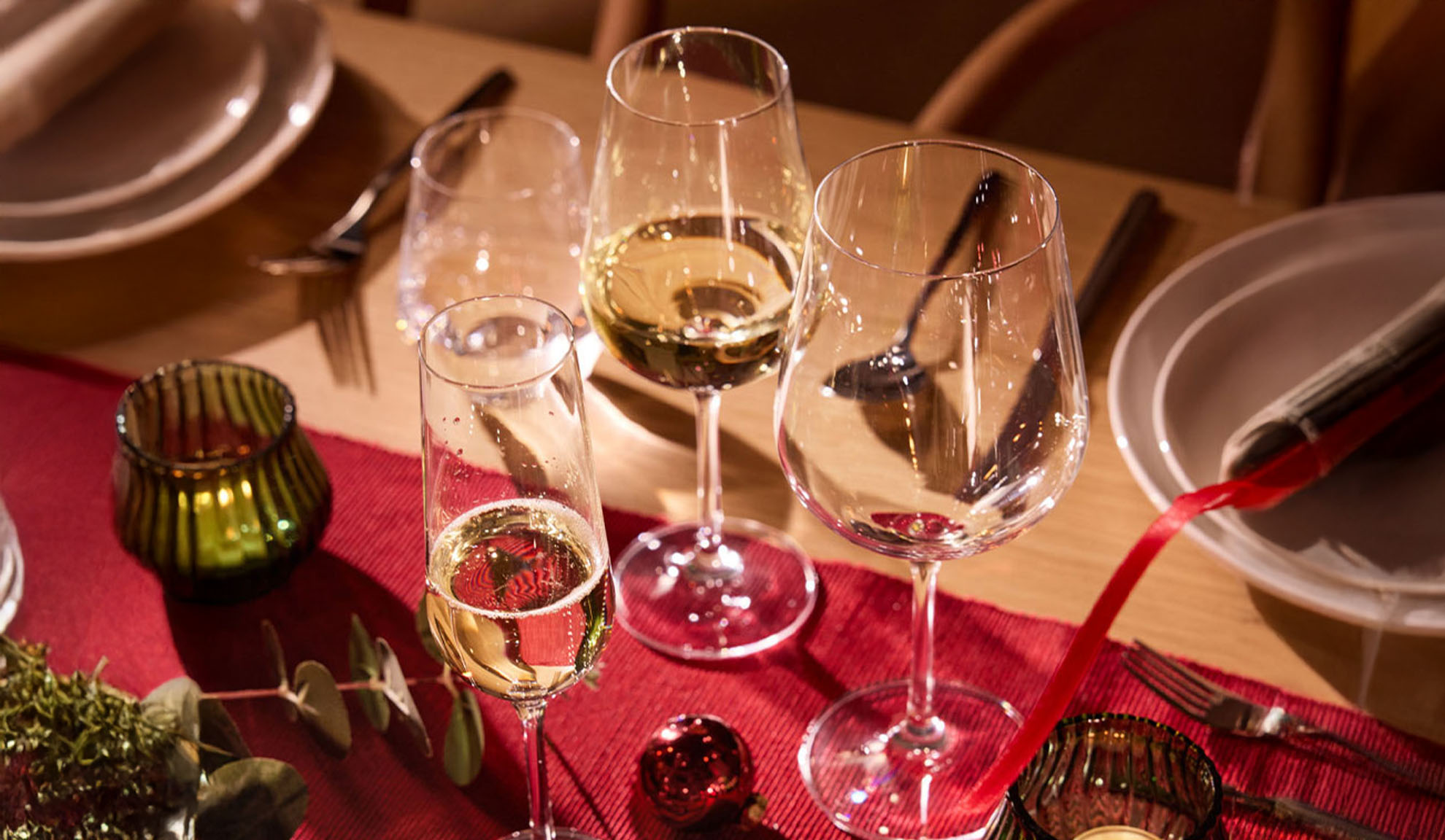 Festligt dukat bord med vinglas, champagneglas och juldekorationer.