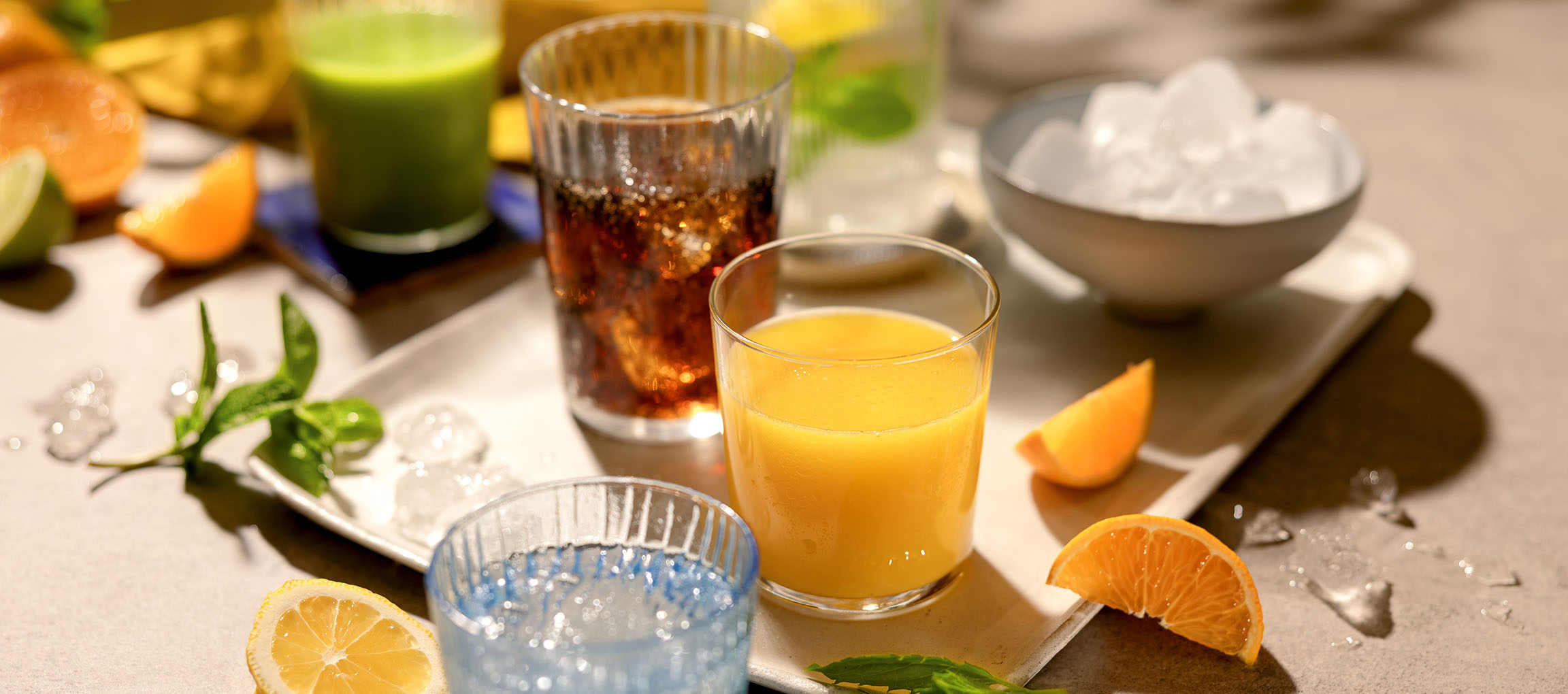 Olika uppfriskande drycker och frukter på en bricka, inklusive apelsinjuice och kolsyrade drycker.