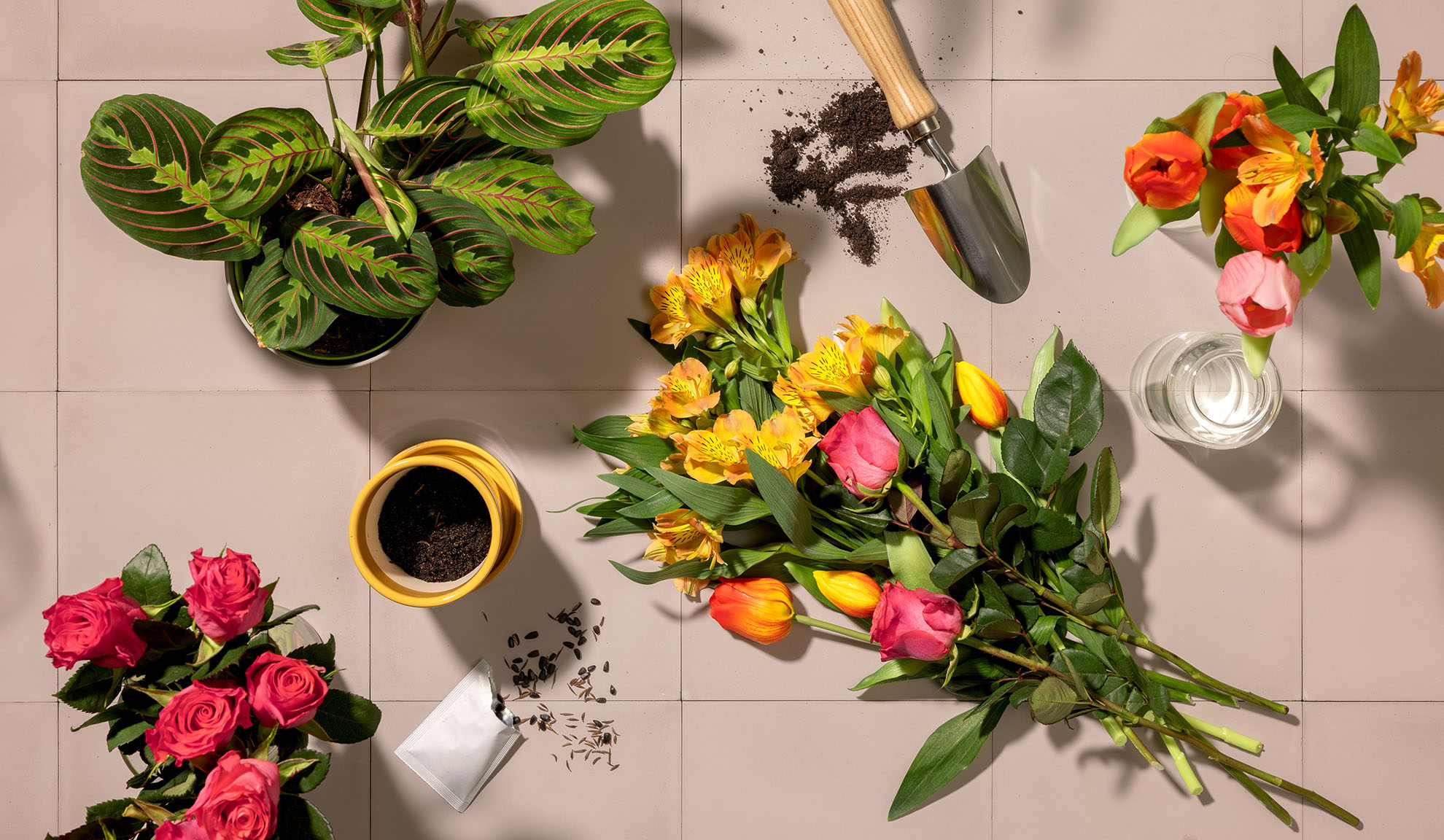 Överblick av trädgårdsredskap, krukväxter och buketter av färgglada blommor på en kaklad yta.
