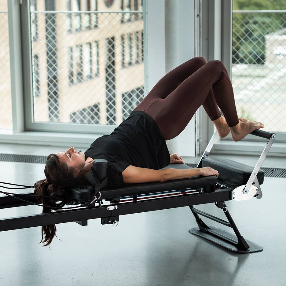 Kvinna tränar pilates på en reformer-maskin, med benen uppåt.