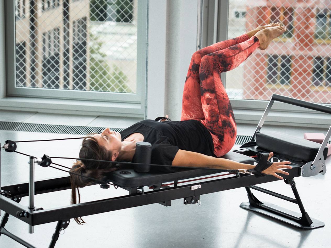 Kvinna som tränar Pilates på en reformer, i röda och svarta leggings