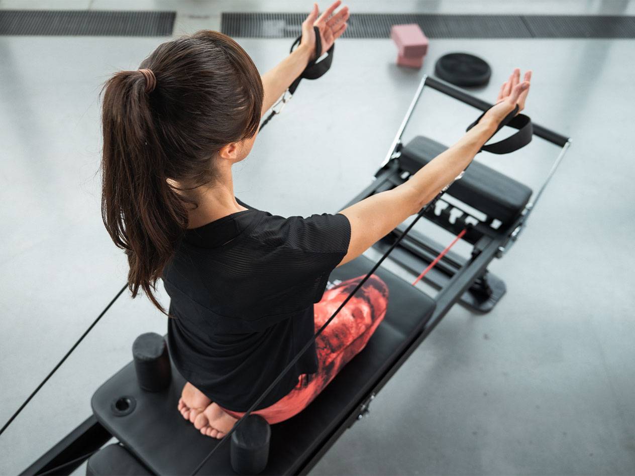 Kvinna tränar pilates på en reformer-maskin med motståndsband.