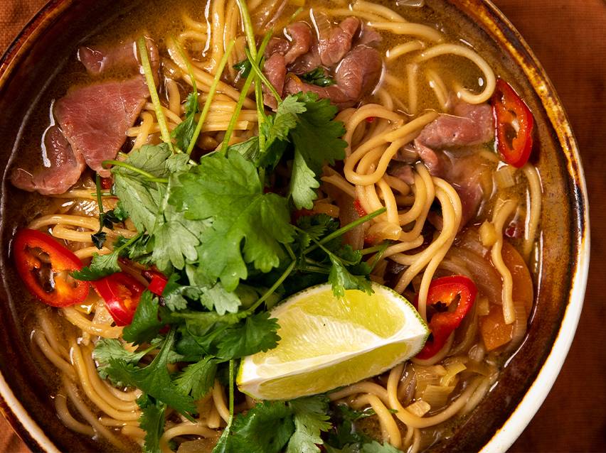 Nudelsoppa med nötkött, garnerad med koriander och lime.