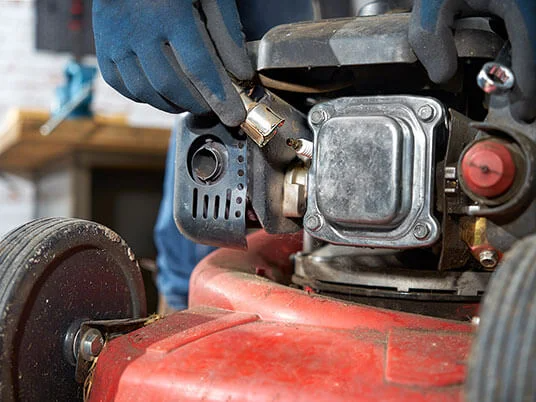Handskar som byter tändstift på en röd gräsklippare.