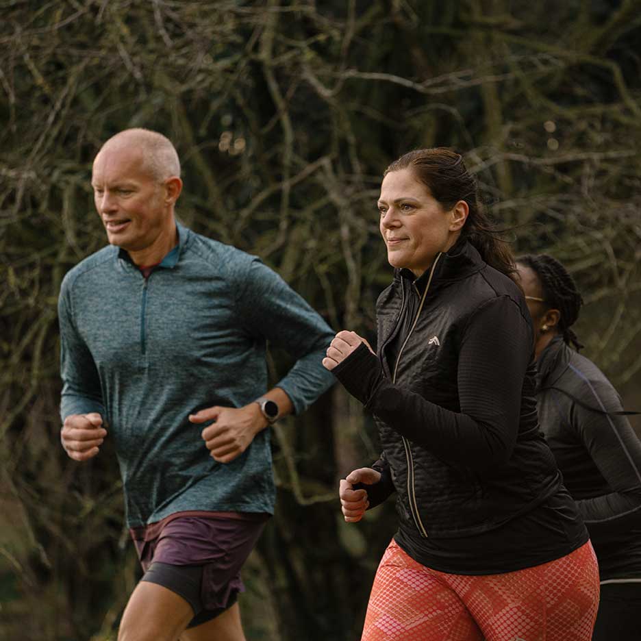 Två vuxna löpare i träningskläder joggar utomhus.