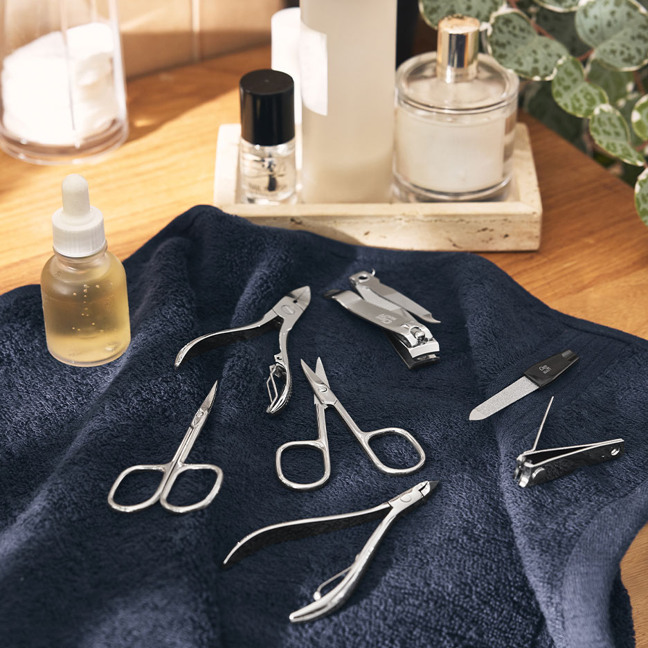 Manikyrset med nagelklippare, saxar och filar på en mörkblå handduk.