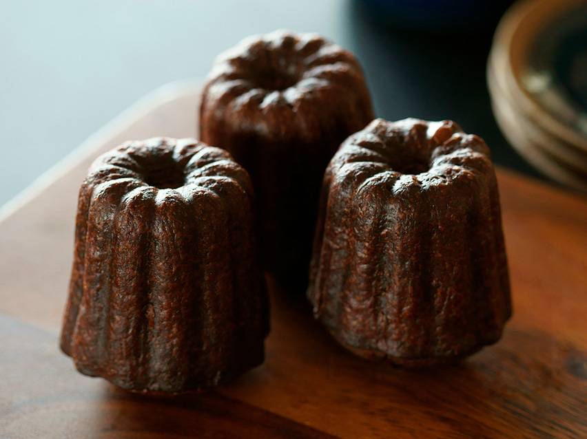 Tre canelés de Bordeaux på en träskiva.
