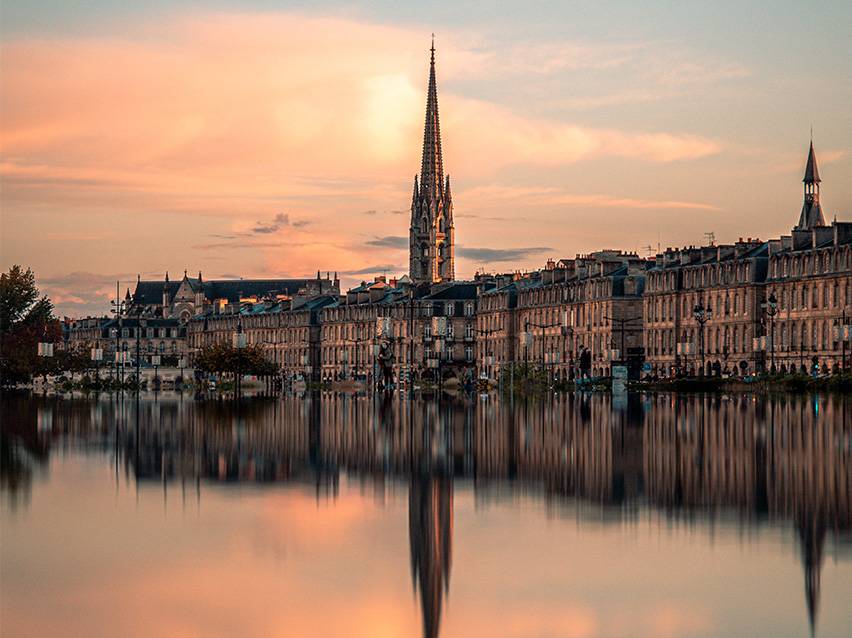 Bordeaux stadsbild vid solnedgången med en kyrka och dess spegelbild i vattnet.