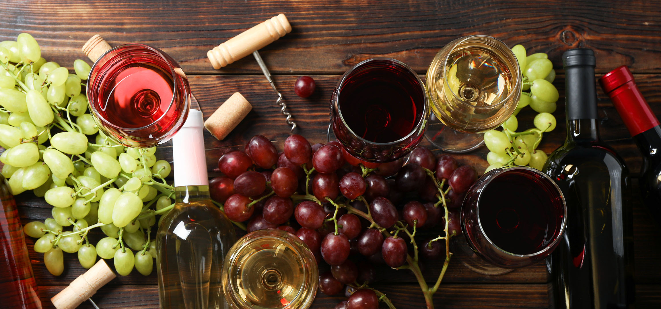 Olika viner, druvor och vintillbehör på ett träbord.