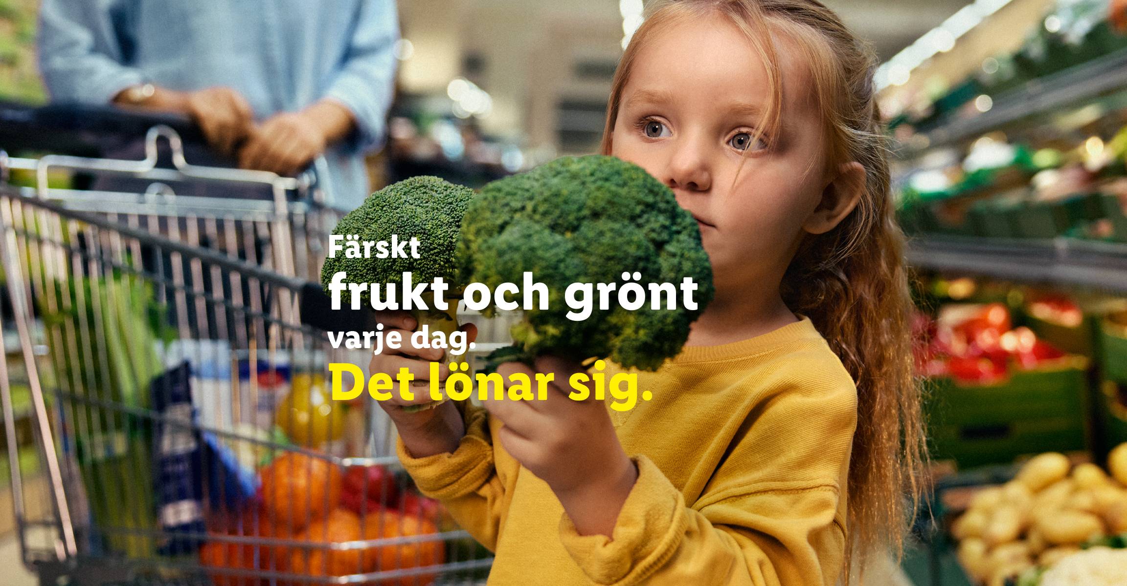Ett barn håller i broccoli i en mataffär med texten 'Färskt frukt och grönt varje dag. Det lönar sig.'