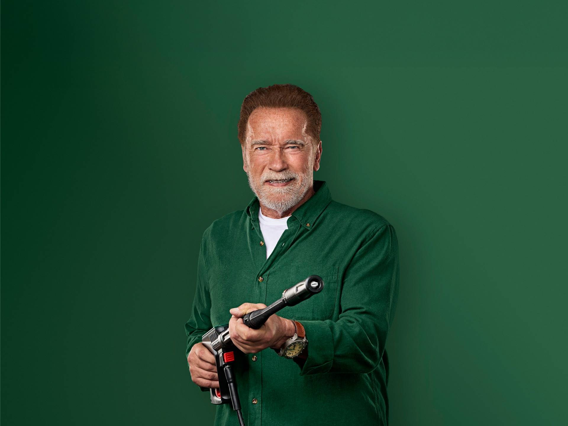 Arnold Schwarzenegger ler, hållande en högtryckstvättspistol.