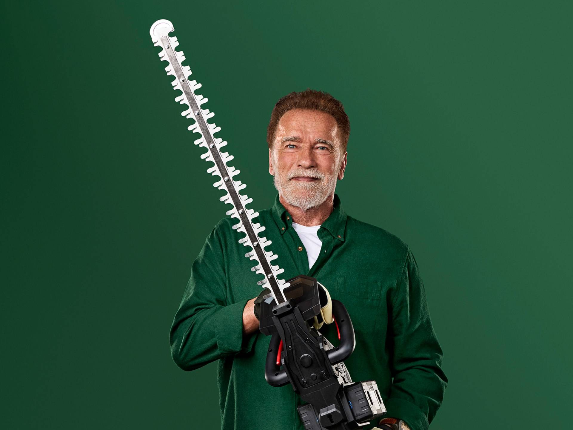 Arnold Schwarzenegger håller en stor häcksax mot en grön bakgrund.