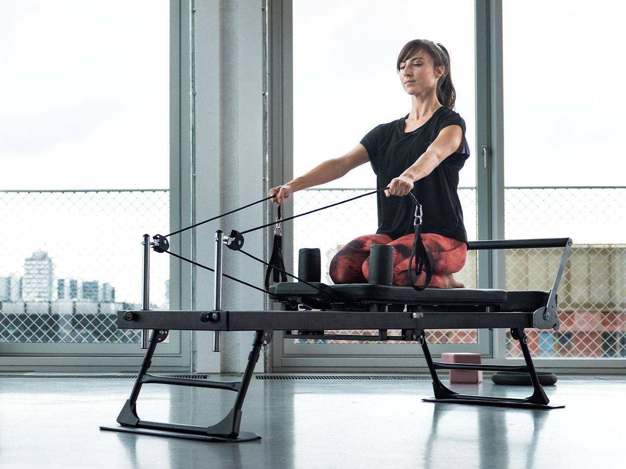 Kvinna som tränar Pilates på en reformer-maskin med stadsbakgrund.
