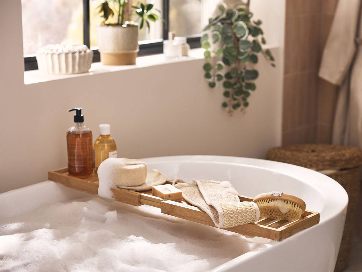 Bambubadbricka med badprodukter, svampar och borstar över ett bubbelbad.