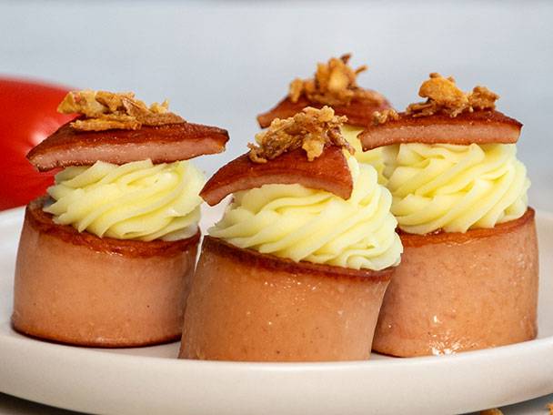 Fyra korvbitar med potatismos och stekt lök på en vit tallrik.