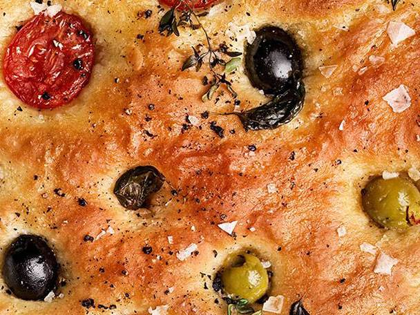 En närbild av focaccia med soltorkade tomater, oliver och timjan.