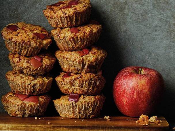 En hög med äppelmuffins står bredvid ett rött äpple.