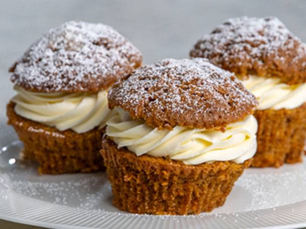 Tre morotsmuffins med gräddostfrosting och florsocker på en vit tallrik.