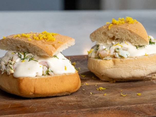 Två räksmörgåsar med majonnäs och dill på en träskärbräda.