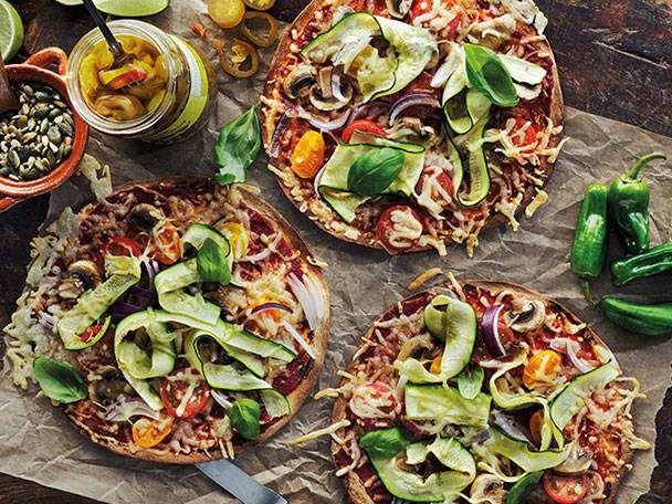 Tre vegetariska pizzor med zucchini, champinjoner och tomater på bakplåtspapper.
