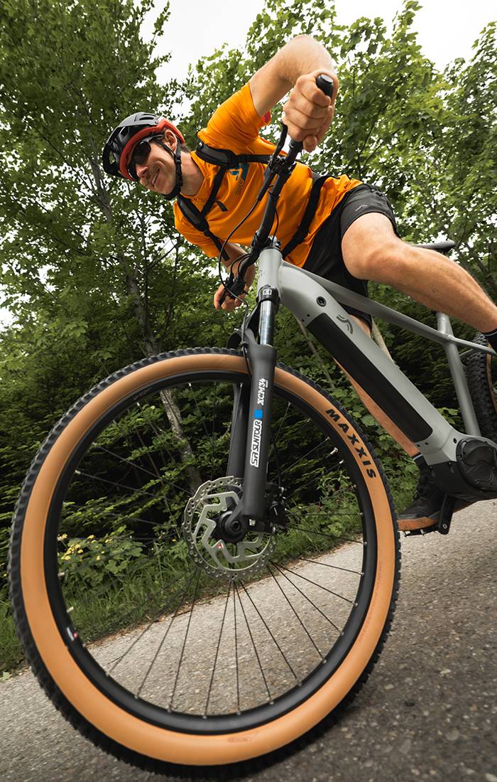 En man cyklar på en grå elcykel Maxxis i en skog.