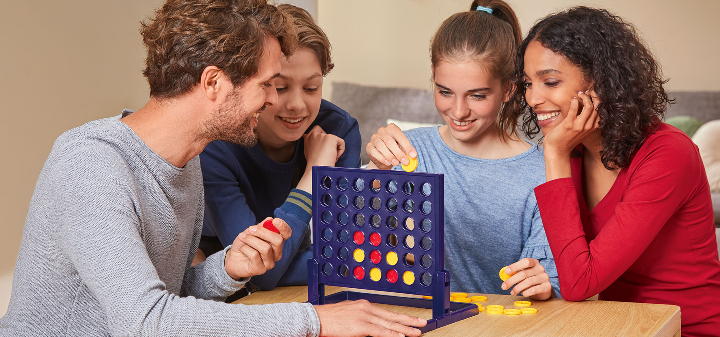 Fyra personer spelar brädspelet Connect 4 vid ett träbord.