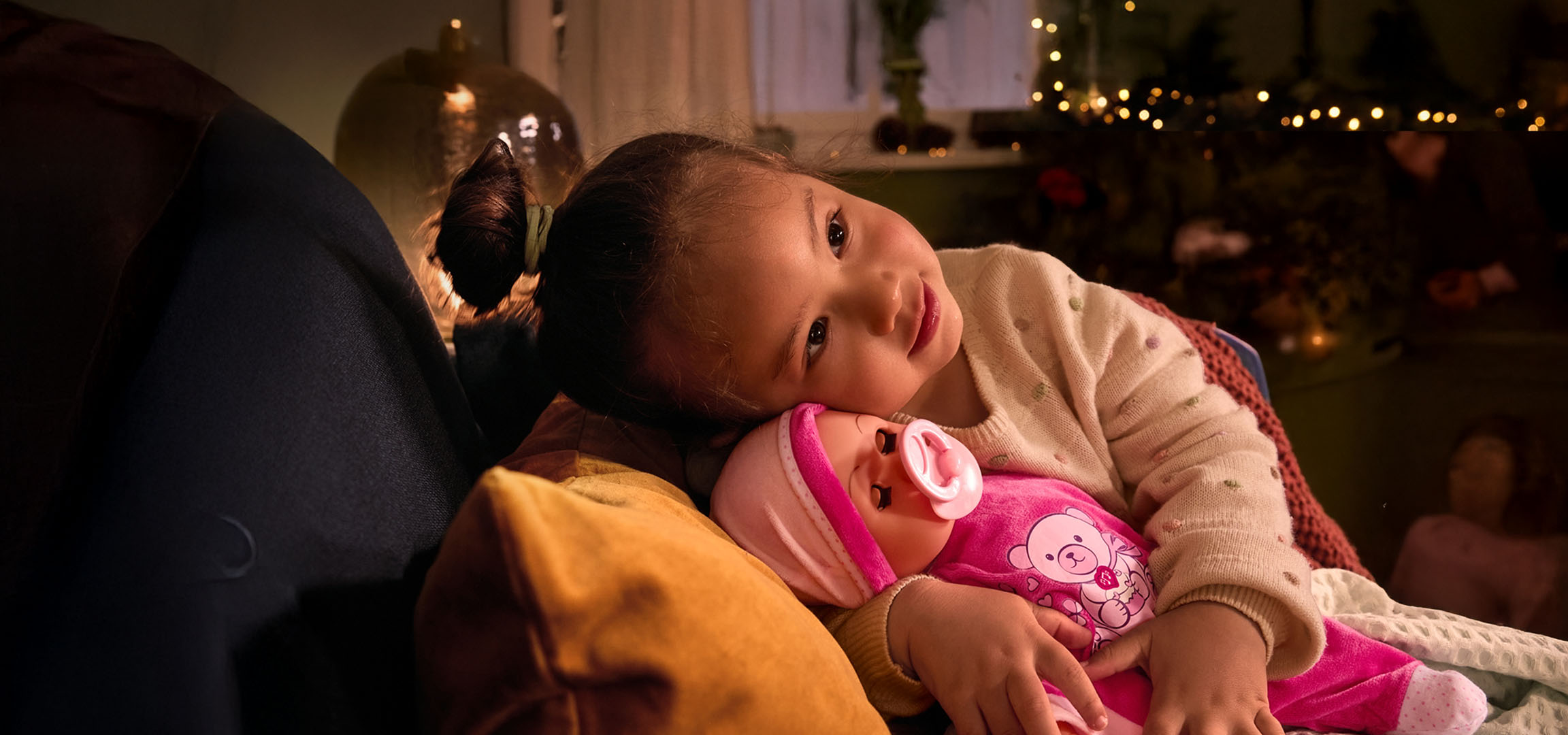 Flicka med docka och napp, mysigt placerad på en kudde.