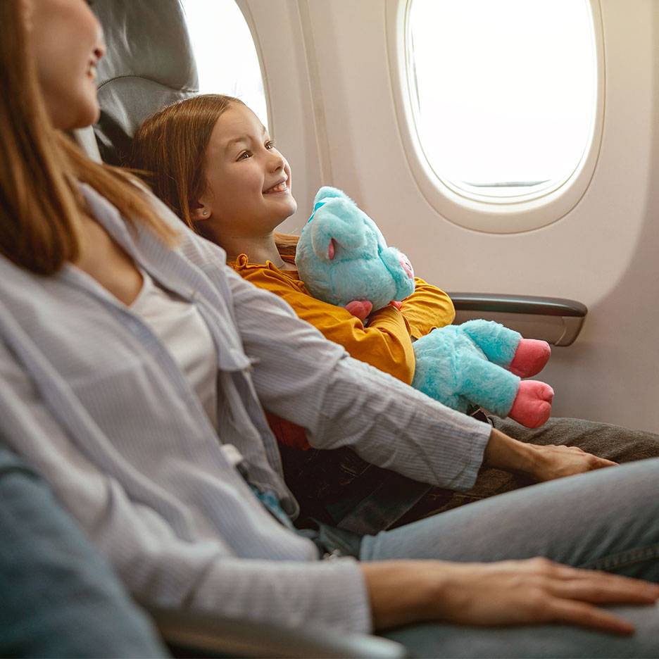 Ett barn med en mjukisleksak tittar ut genom ett flygplansfönster bredvid en vuxen.