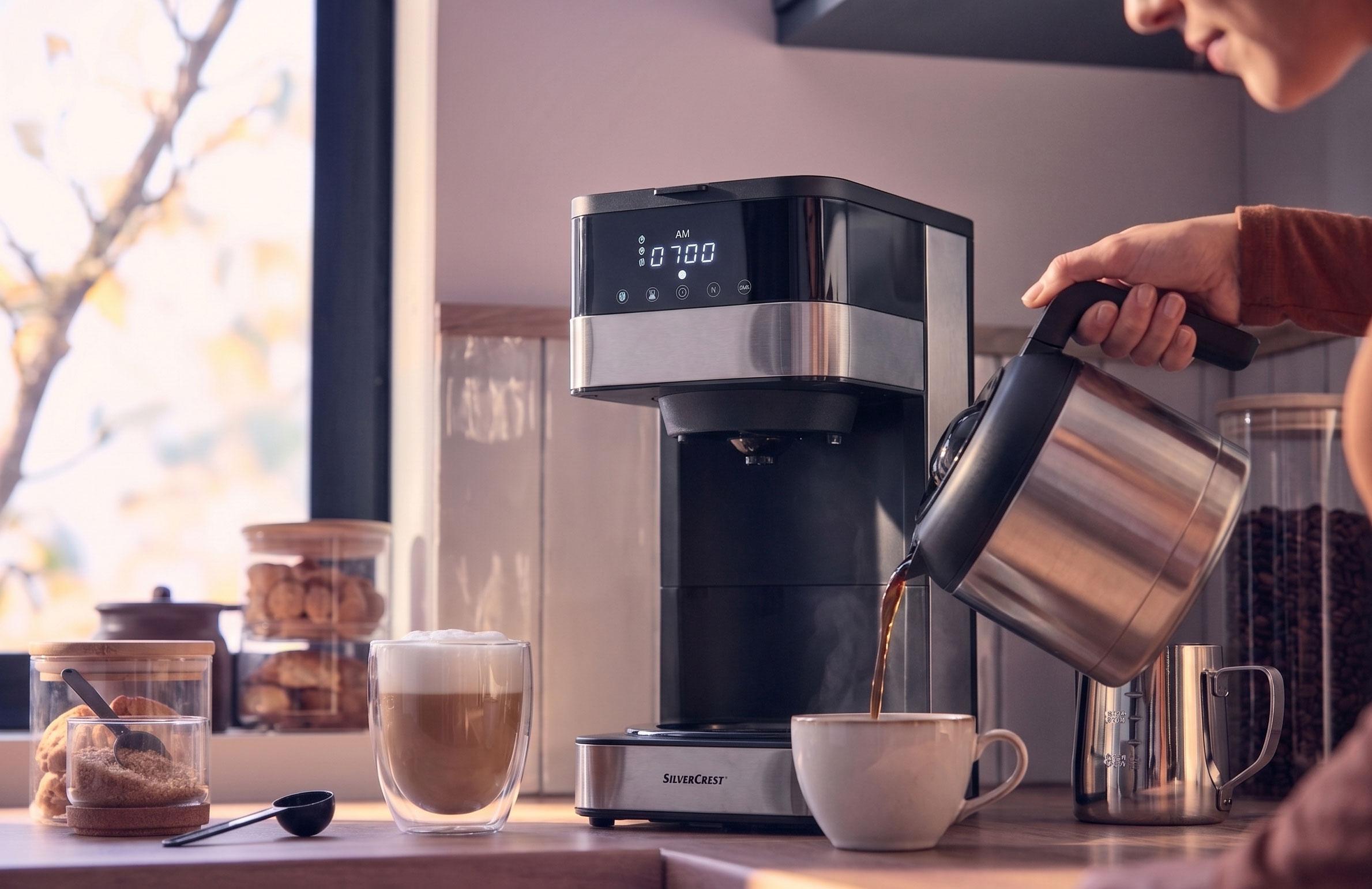 Kaffemaskin häller kaffe i en kopp, med en latte och kakor på bänken.