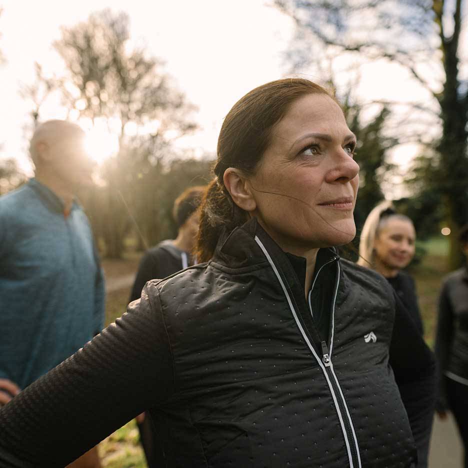 Kvinna i svart sportjacka tittar uppåt, med en grupp människor i bakgrunden.