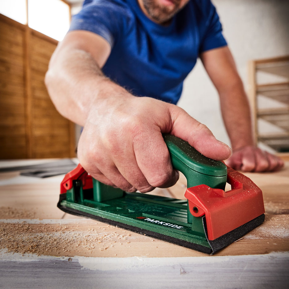 Man slipar en träyta med en handslipmaskin, med sågspån runt omkring.