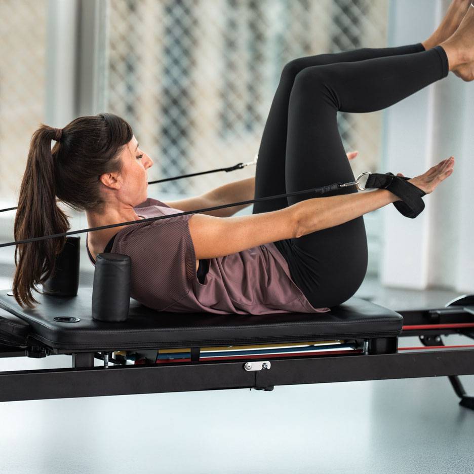Kvinna tränar pilates på en reformer med svarta träningskläder.