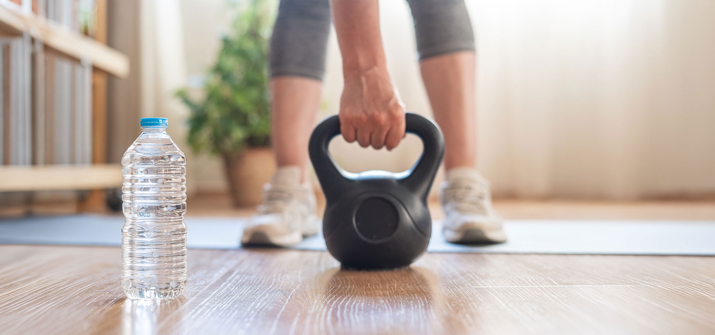 aiLabeling.aiLabelForImageAltText: Kvinna förbereder sig för att träna med en kettlebell och vattenflaska på en yogamatta.