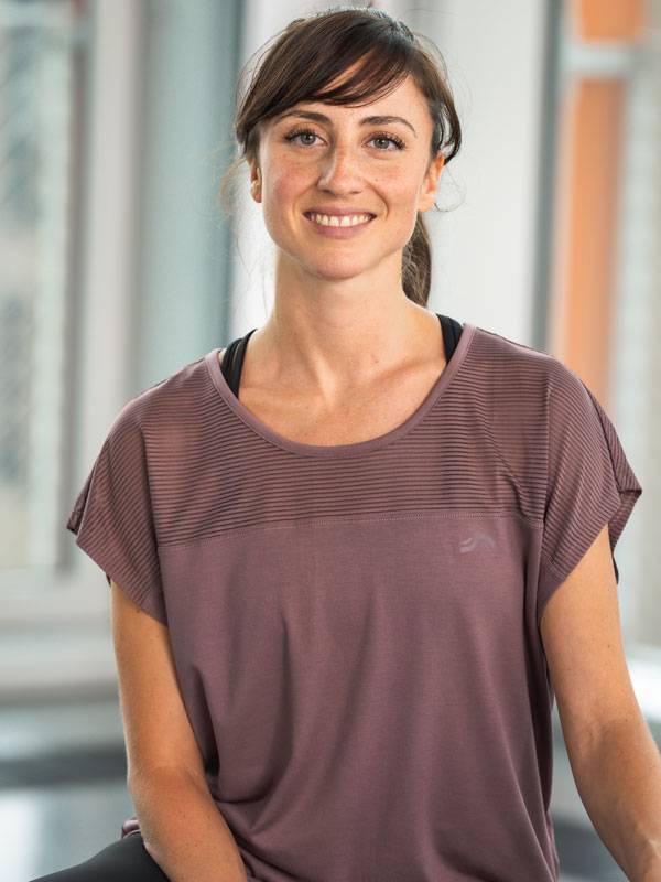 Kvinna i en lila sporttopp med korta ärmar, leende.